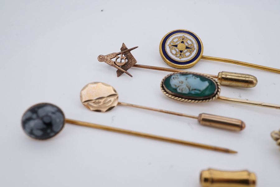 A collection of six stick pins, comprising: three gold stick pins, one set with a hardstone cameo, Austrian assay marks; a gold stick pin with a faceted edge; and a gold stick pin of Masonic design, stamped 9CT, combined